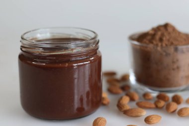 Badem çikolatası, bol badem ve pürüzsüz çikolata karışımı. Afiyet olsun kahvaltıları için mükemmel. Etrafında bademler ve arka planda bir kase kakao tozu ile vurulmuş.