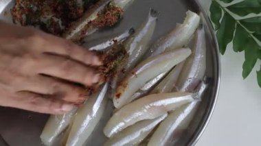 Baharat için taze kesilmiş ve temizlenmiş ançüez balığının yanında acı biber tozu, biber, zencefil sarımsak ezmesi ve tuz ile birlikte taze köri yapraklarıyla çevrili bir tabakta sunulması.. 