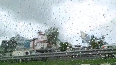 Yağmur, arka araba penceresinden manzarayı bozdu. Yağmur damlaları, Pune 'a giden yolda geçen araçların ve yüksek binaların görüntüsünü neşeli bir şekilde bozdu.