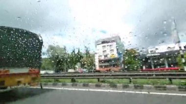 Pune, Hindistan, 15 Haziran 2024: Yağmur, yağmur damlalarının Pune 'a giden yoldaki araç ve otoyol binalarını eğlenceli bir şekilde çarpıttığı arka araba penceresinden manzarayı karaladı.