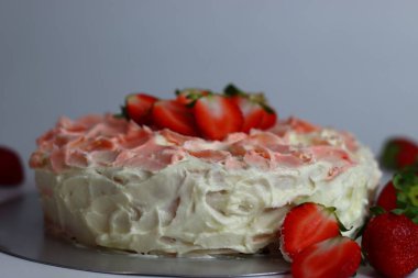 Gül pembesi kremalı ve çiçek yapraklı taze çilek dilimleriyle kaplı tereyağlı çilekli kek. Tatlı severler, özel günler ve kutlamalar için ideal. Görsel olarak büyüleyici bir fotoğraf.