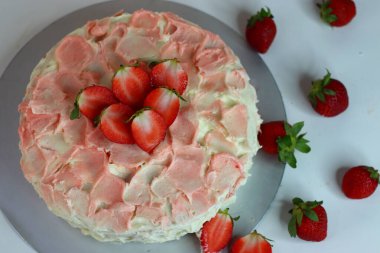 Gül pembesi kremalı ve çiçek yapraklı taze çilek dilimleriyle kaplı tereyağlı çilekli kek. Tatlı severler, özel günler ve kutlamalar için ideal. Görsel olarak büyüleyici bir fotoğraf.