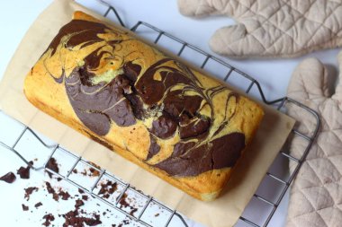 Taze pişmiş mermer kek, tel askıda soğuyor, karışık çikolata ve vanilya kıvrımları sergiliyor. Parşömen kağıdına serpiştirilmiş kırıntılar, kırsal cazibe ve hoşgörüyü somutlaştırıyor.