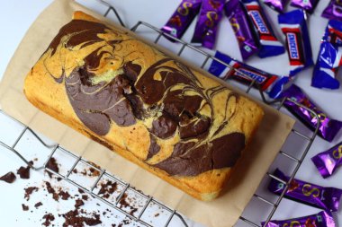 Mumbai, Hindistan, 14 Şubat 2025: Mini Snickers ve Cadbury çikolatalarıyla çevrili soğutma rafında çikolata ve vanilyalı taze pişmiş mermer pasta.