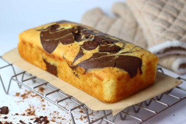 Taze pişmiş mermer kek, tel askıda soğuyor, karışık çikolata ve vanilya kıvrımları sergiliyor. Parşömen kağıdına serpiştirilmiş kırıntılar, kırsal cazibe ve hoşgörüyü somutlaştırıyor.