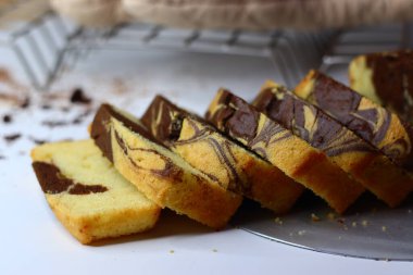 Beyaz bir yüzeye yerleştirilmiş çikolatalı ve vanilyalı mermer pasta dilimleri. Dağınık kakao tozu ve çikolata talaşları çekiciliğini artırıyor ve bu görüntüyü kırsal tatlılar için mükemmel yapıyor.