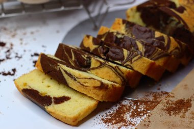 Beyaz bir yüzeye yerleştirilmiş çikolatalı ve vanilyalı mermer pasta dilimleri. Dağınık kakao tozu ve çikolata talaşları çekiciliğini artırıyor ve bu görüntüyü kırsal tatlılar için mükemmel yapıyor.