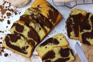 Beyaz bir yüzeye yerleştirilmiş çikolatalı ve vanilyalı mermer pasta dilimleri. Dağınık kakao tozu ve çikolata talaşları çekiciliğini artırıyor ve bu görüntüyü kırsal tatlılar için mükemmel yapıyor.