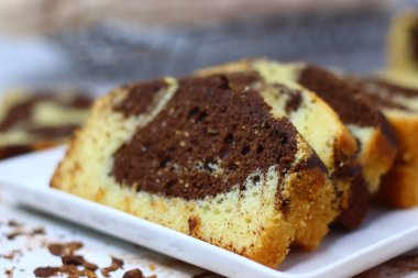 Beyaz bir yüzeye yerleştirilmiş çikolatalı ve vanilyalı mermer pasta dilimleri. Dağınık kakao tozu ve çikolata talaşları çekiciliğini artırıyor ve bu görüntüyü kırsal tatlılar için mükemmel yapıyor.