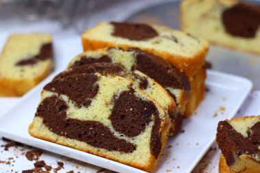 Beyaz bir yüzeye yerleştirilmiş çikolatalı ve vanilyalı mermer pasta dilimleri. Dağınık kakao tozu ve çikolata talaşları çekiciliğini artırıyor ve bu görüntüyü kırsal tatlılar için mükemmel yapıyor.