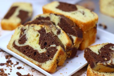 Beyaz bir yüzeye yerleştirilmiş çikolatalı ve vanilyalı mermer pasta dilimleri. Dağınık kakao tozu ve çikolata talaşları çekiciliğini artırıyor ve bu görüntüyü kırsal tatlılar için mükemmel yapıyor.