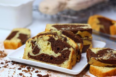 Beyaz bir yüzeye yerleştirilmiş çikolatalı ve vanilyalı mermer pasta dilimleri. Dağınık kakao tozu ve çikolata talaşları çekiciliğini artırıyor ve bu görüntüyü kırsal tatlılar için mükemmel yapıyor.