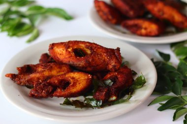 Vietnam inci benekli balığı aromatik baharatlarla marine edilmiş ve altın mükemmelliğinde kızartılmış taze köri yapraklarıyla süslenmiş. Üst taraftan çekilen, zengin dokusunu ve canlı tonlarını vurguluyor.