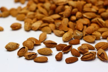 Kabukları beyaz bir yüzeye saçılmış çiğ bademler doğal dokularını ve toprak tonlarını sergiliyor. Sağlıklı yağ, protein ve vitamin içeren bademler kalp sağlığı ve beyin fonksiyonlarını destekler.