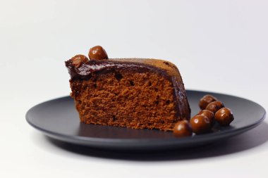 Parlak çikolata ganache ve çikolata kaplı fındıklarla kaplı zengin, nemli çikolatalı kek dilimi. Premium kakao ve bademlerden yapılmış, antioksidan ve sağlıklı yağ sunuyor.