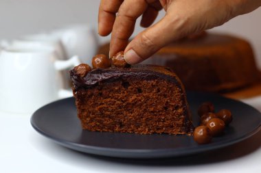 Parlak çikolata ganache ve çikolata kaplı fındıklarla kaplı zengin, nemli çikolatalı kek dilimi. Premium kakao ve bademlerden yapılmış, antioksidan ve sağlıklı yağ sunuyor.