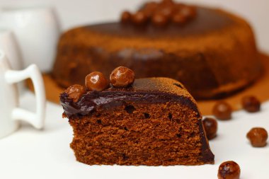 Parlak çikolata ganache ve çikolata kaplı fındıklarla kaplı zengin, nemli çikolatalı kek dilimi. Premium kakao ve bademlerden yapılmış, antioksidan ve sağlıklı yağ sunuyor.