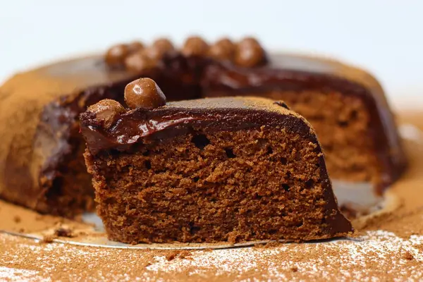 Parlak çikolata ganache ve çikolata kaplı fındıklarla kaplı zengin, nemli çikolatalı kek dilimi. Premium kakao ve bademlerden yapılmış, antioksidan ve sağlıklı yağ sunuyor.