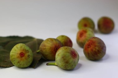 Beyaz arka planda yeşil yapraklı taze incirler. Yüksek miktarda lif, antioksidan ve vitamin sindirime ve sağlığa yardımcı olur. Gıda blogları, beslenme alanları ve stok fotoğrafçılığı için ideal.