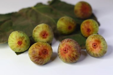 Beyaz arka planda yeşil yapraklı taze incirler. Yüksek miktarda lif, antioksidan ve vitamin sindirime ve sağlığa yardımcı olur. Gıda blogları, beslenme alanları ve stok fotoğrafçılığı için ideal.