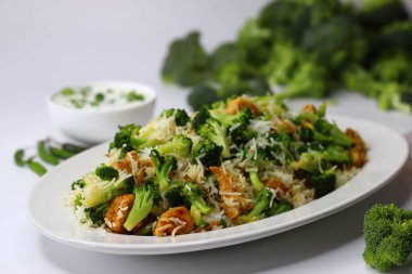 Raita ile brokoli tavuklu pilav. Yumuşak kızarmış tavuk, taze brokoli ve kremalı raita ile servis edilen yumuşacık pilav içeren besleyici bir yemek. Protein, lif ve soğutma lezzetleriyle dolu.