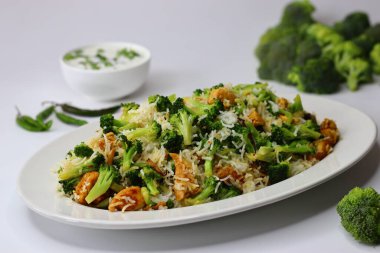 Raita ile brokoli tavuklu pilav. Yumuşak kızarmış tavuk, taze brokoli ve kremalı raita ile servis edilen yumuşacık pilav içeren besleyici bir yemek. Protein, lif ve soğutma lezzetleriyle dolu.