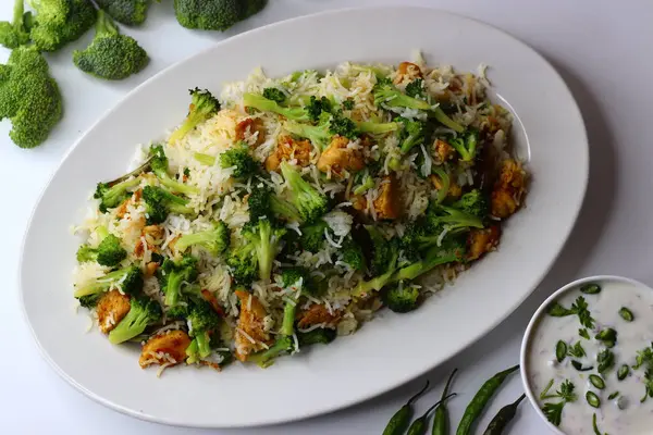 Raita ile brokoli tavuklu pilav. Yumuşak kızarmış tavuk, taze brokoli ve kremalı raita ile servis edilen yumuşacık pilav içeren besleyici bir yemek. Protein, lif ve soğutma lezzetleriyle dolu.
