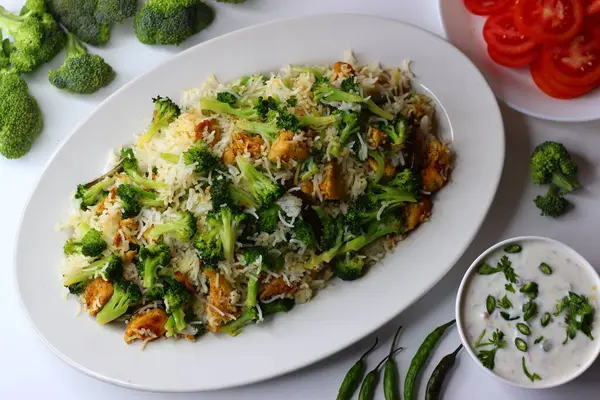 Raita ile brokoli tavuklu pilav. Yumuşak kızarmış tavuk, taze brokoli ve kremalı raita ile servis edilen yumuşacık pilav içeren besleyici bir yemek. Protein, lif ve soğutma lezzetleriyle dolu.