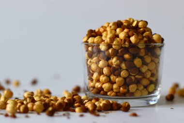 Crispy Roasted Channa chickpeas in a glass, scattered on white background. Perfect for Indian snacks, protein rich diets, and healthy eating themes. Ideal for clean eating and vegan food imagery