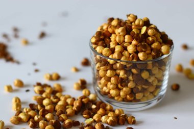 Crispy Roasted Channa chickpeas in a glass, scattered on white background. Perfect for Indian snacks, protein rich diets, and healthy eating themes. Ideal for clean eating and vegan food imagery