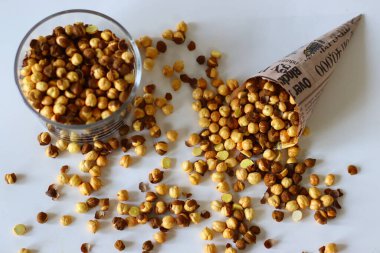 Crispy Roasted Channa chickpeas in a glass and in newspaper cone, scattered on white background. Perfect for Indian snacks, protein rich diets, and healthy eating themes