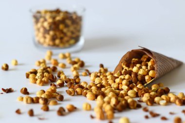 Crispy Roasted Channa chickpeas in a glass and in newspaper cone, scattered on white background. Perfect for Indian snacks, protein rich diets, and healthy eating themes