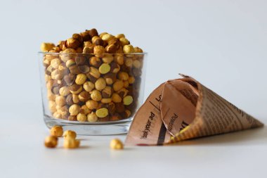 Crispy Roasted Channa chickpeas in a glass and in newspaper cone, scattered on white background. Perfect for Indian snacks, protein rich diets, and healthy eating themes