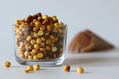 Crispy Roasted Channa chickpeas in a glass and in newspaper cone, scattered on white background. Perfect for Indian snacks, protein rich diets, and healthy eating themes