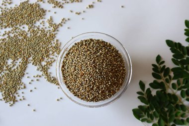 Taze moringa yaprakları ve temiz beyaz zemine dizilmiş bir kase bajra ya da inci darı. Vegan, Ayurvedic ve Güney Hindistan mutfağı için ideal yemek fotoğrafçılığı.