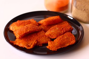 Çiğ tilapia filetosu koyu Hint baharatı karışımı kırmızı biber, zerdeçal, biber ve tuz ile marine edilmiş, siyah bir tabakta. Ev yapımı balık körisi, desi mutfağı ya da lezzetli deniz ürünleri hazırlamak için ideal.