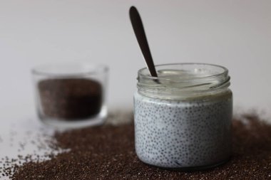 Kavanozda Chia 'ya batırılmış süt ya da chia pudingi, etrafa saçılmış chia tohumları ve bir kap kuru tohumla çevrili. Sağlıklı görseller, kahvaltı temaları ve beslenme içeriği için iyi bir kremalı vegan yemeği.