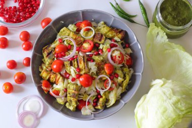 Lezzetli ve canlı paneer salatası içinde ızgara paneer küpleri, kiraz domatesleri, nar tohumları, dilimlenmiş soğanlar ve gri bir kasede doğranmış marul var. Sağlıklı Hint aşıkları için mükemmel..