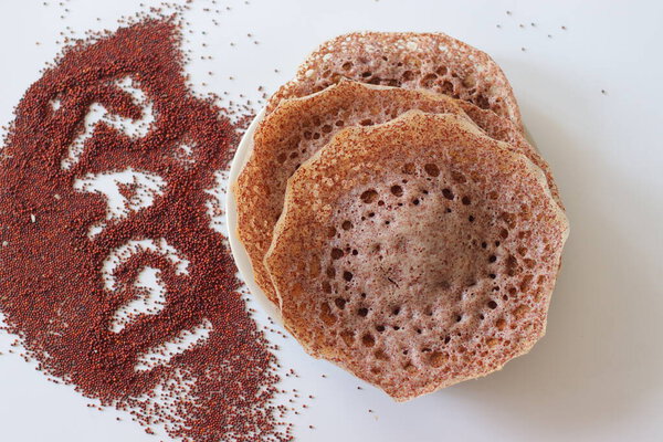 Ragi appams with crisp edges and soft center served on a ceramic plate, made from fermented finger millet batter. Styled with scattered millets on a white backdrop, an authentic South Indian breakfast