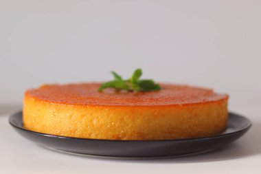 Karamelli ekmek pudingi, parlak kehribar kaplı, taze nane yapraklarıyla süslenmiş ve siyah bir tabakta servis ediliyor. Ekmek, yumurta, süt ve karamelize şekerden yapılmış zengin bir Anglo-Hindistan tatlısıdır.