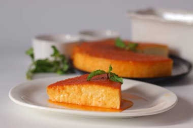 Beyaz bir tabakta servis edilen bir dilim karamelli puding, üzerine taze nane ve üzerine altın karamel sosu serpilmiş. Ekmek, yumurta, süt ve şekerden yapılmış zengin bir İngiliz-Hint tatlısıdır.