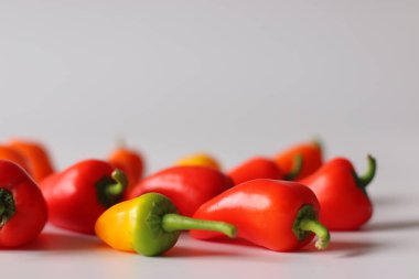Yeşil saplı canlı kırmızı, turuncu ve sarı kozaların yer aldığı beyaz bir yüzeyde sunulan mini dolmalık biberler yumuşak doğal ışıkla fotoğraflandı. Renk ve sağlıklı yemek temaları için ideal