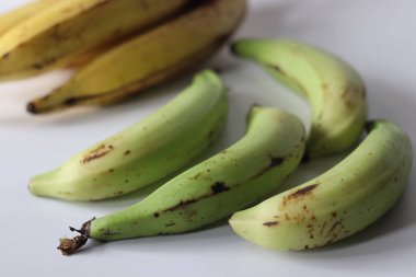Çiğ ve olgun Nendran tohumları, yeşil ve sarı derili doğal tomurcuklar içinde yan yana tutulur. Olgunlaşan aşamaların görüntüsü. Tropikal hasat ve mutfak kontrastı temaları için ideal