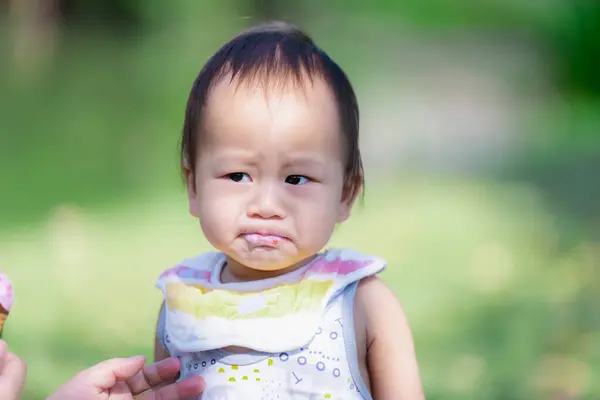 一年大的亚洲男婴吃了甜酸苦辣的草莓冰淇淋 孩子们穿上杏仁 幼儿们吃着糖果后 表情严肃 — 图库照片