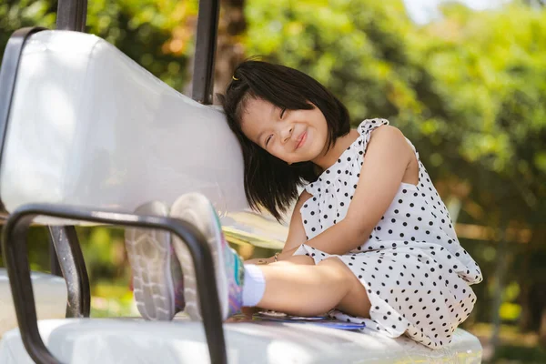 Smiling Girl Enjoying a Relaxing Moment Outdoors, Cheerful Kid aged 6 years old with a big smile sits comfortably in golf cart, enjoying relaxing moment in the warm, sunlit ambiance of peaceful park.