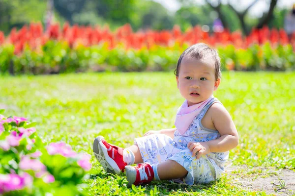 1岁的亚洲花童坐在五彩缤纷的花园中 小孩子若有所思地坐在草地上 四周是五颜六色的花园 展示着童年时代的天真与美丽 — 图库照片