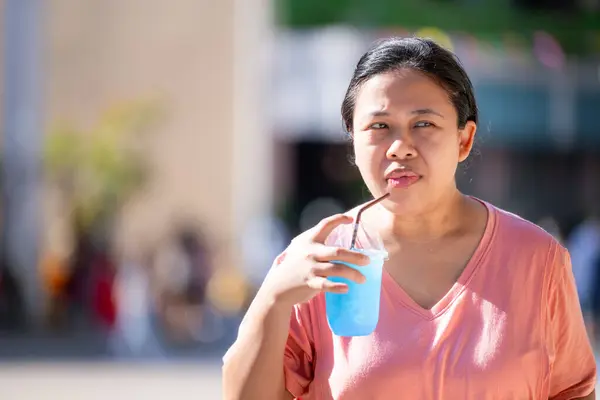 A woman is drinking clear blue soda water in a plastic glass with a straw, on a very hot day, refreshing and thirst-quenching the body. Empty space for entering text.