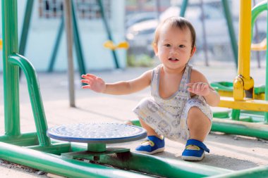 Küçük çocuk güneşli bir yaz gününde oyun parkı egzersiz makinesinde mutlu bir şekilde oynuyor. Tatlı çocuk gülümsüyor. Çocuklar eğlenirken pikabı kaydırmak için küçük ellerini kullanırlar..
