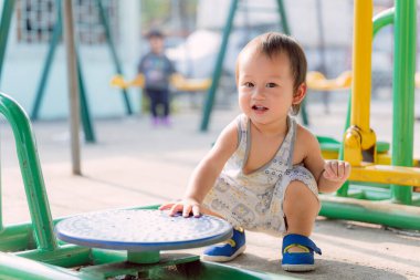 Asyalı küçük çocuk yaz boyunca oyun alanında gülüyor ve eğleniyor, oyun oynayarak öğreniyor. Çocuk dışarıda spor salonunda eğleniyor. Bir yıl altı aylık sevimli bir çocuk yerde oturuyor..