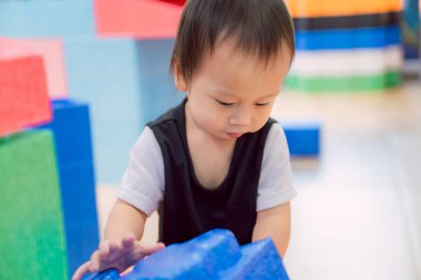 Evde renkli oyuncak bloklarıyla oynayan küçük bir çocuk. Küçük çocuk oyuncaklardan kule inşa ediyor. Bebek ve bebek için eğitici bir oyun. Çocuklar oyuncak ev yapar..